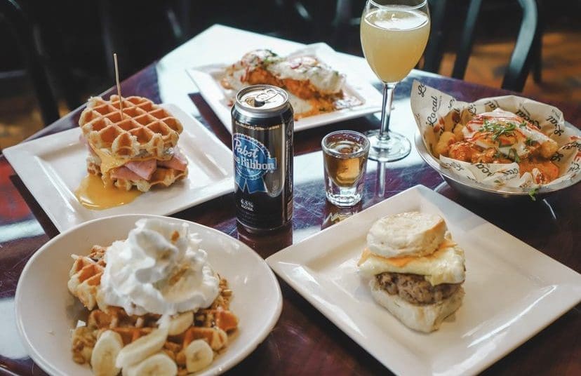 Local on a square brunch that includes mimosas waffles with bananas and a waffle sandwich